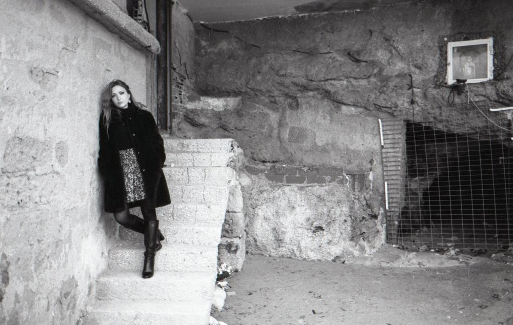 Black and white photograph showing a dark stone tunnel or passageway with rough textured walls and low lighting.