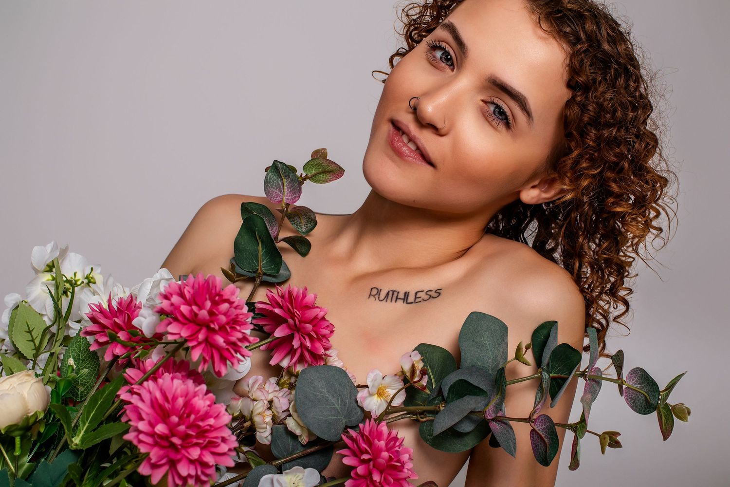 A artistic portrait with pink dahlias and eucalyptus branches against a neutral background.