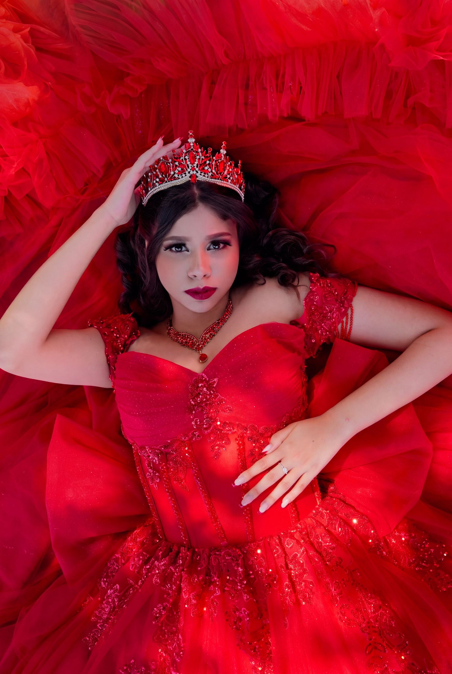 Young woman in red ballgown and jeweled crown poses regally for a quinceañera portrait. Toronto GTA