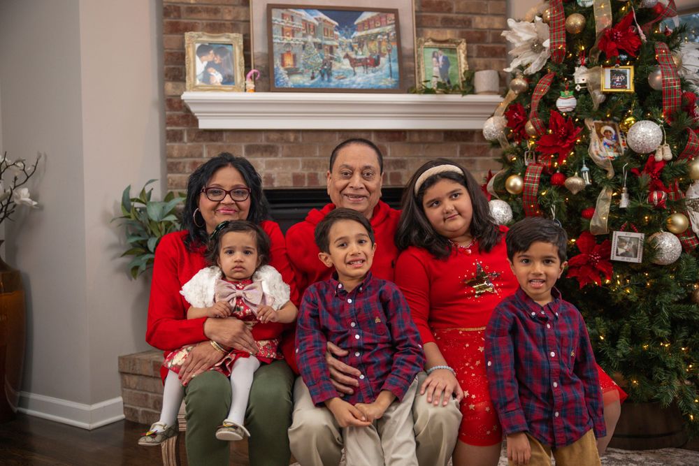 Holiday family photo with decorated Christmas tree and multiple children wearing festive outfits.