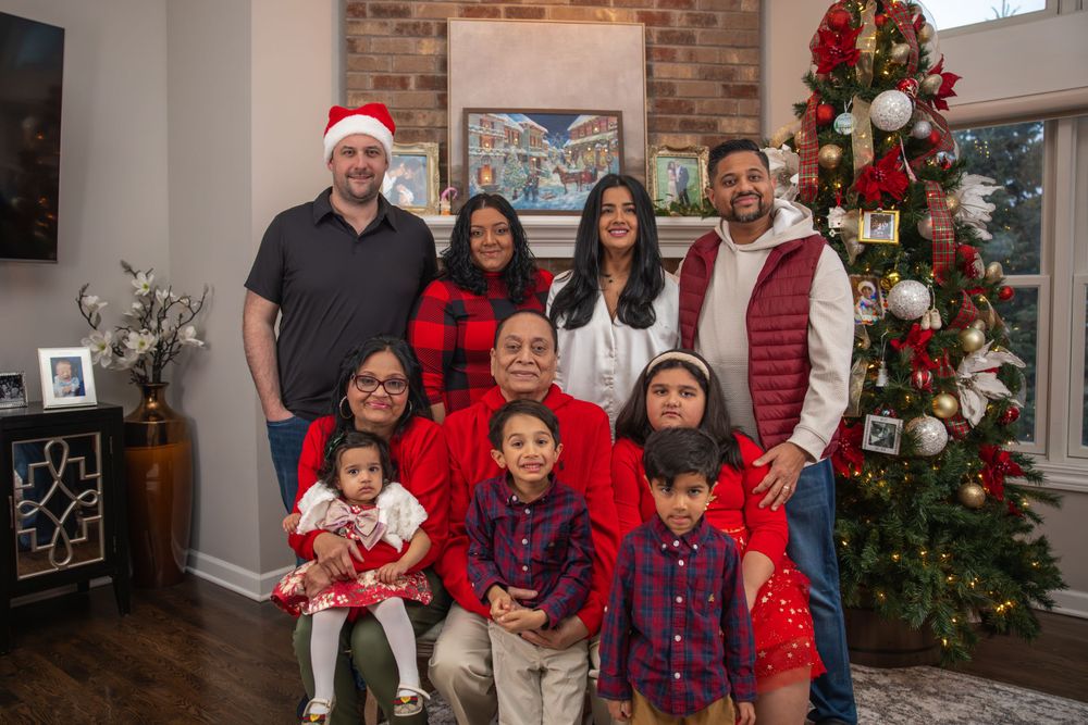 Extended family holiday portrait with Christmas tree, brick fireplace, and matching red and black outfits.