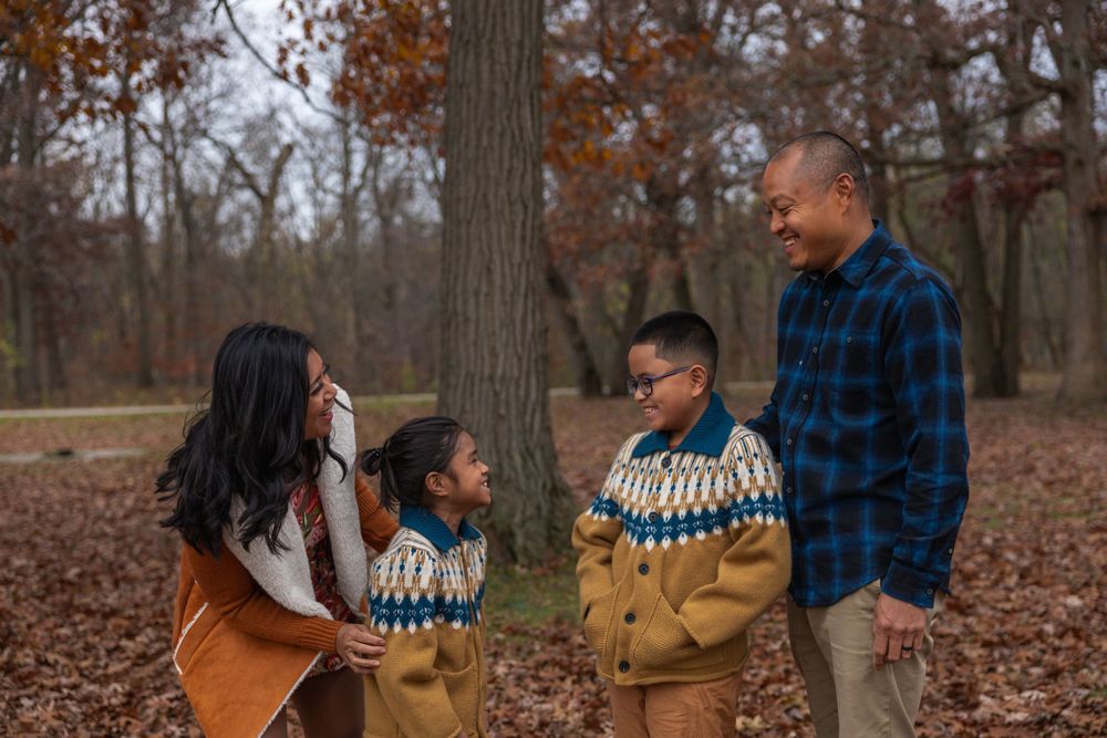 Family sharing playful moment in autumn forest with fallen leaves.