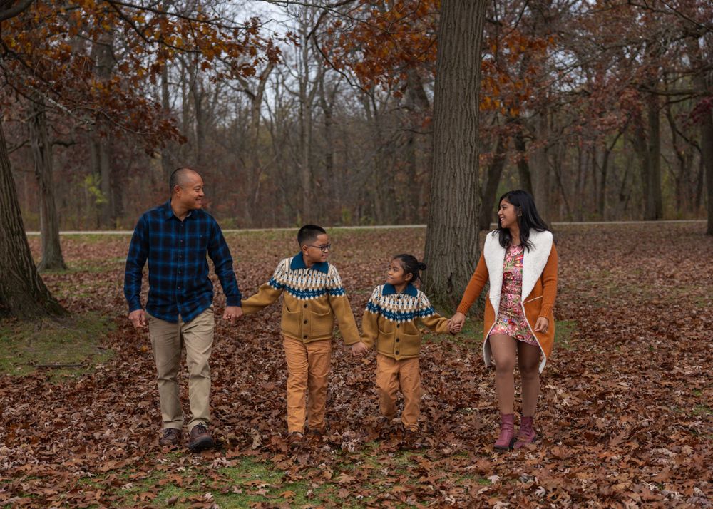 Family walking together through forest covered in fallen autumn leaves.