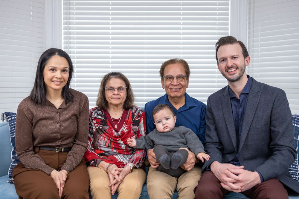 Multi-generational family portrait on a blue couch with infant and grandparents in casual attire.