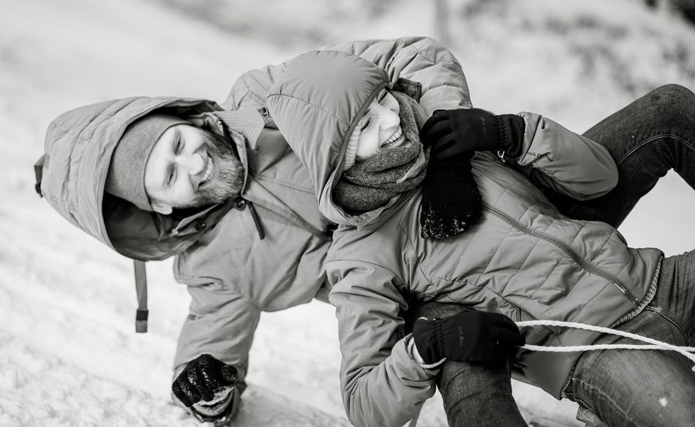 Black and white photo of couple playing and laughing together on a snowy slope.