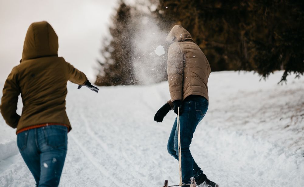 Two people in brown winter jackets walking up a snowy hill through fresh snow.