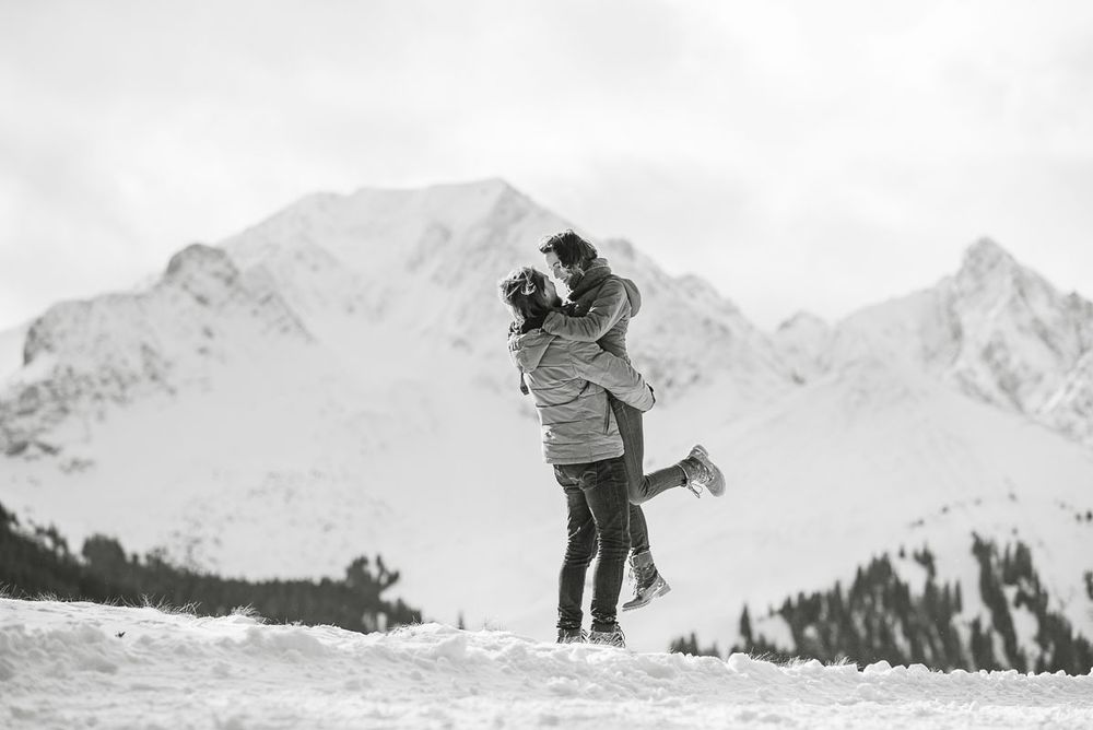 Couple embracing in snowy mountain landscape in black and white winter photography.