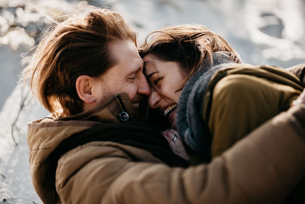 Happy couple laughing and embracing outdoors in warm winter jackets during golden hour.