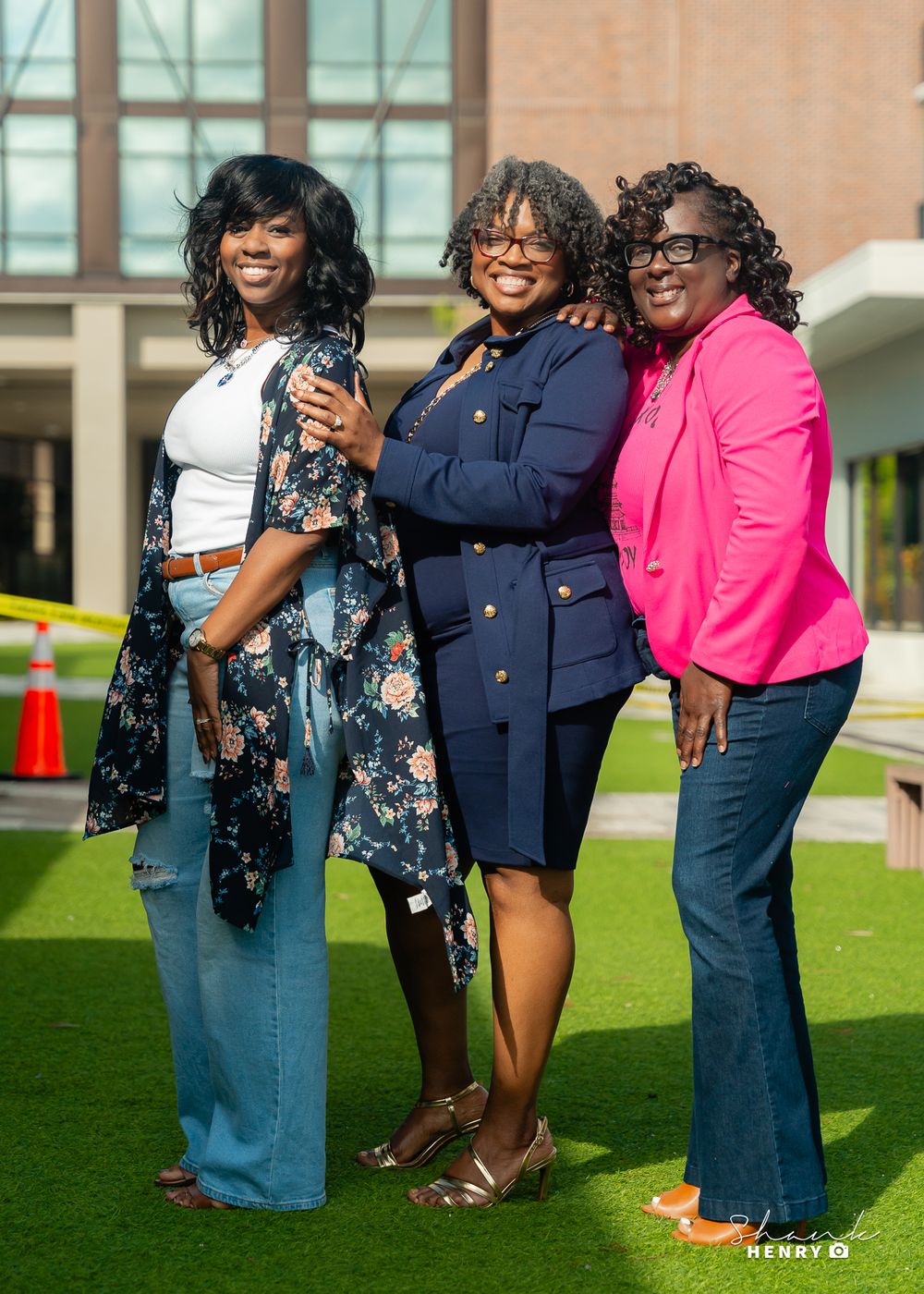 Three people posing together outdoors, wearing coordinated outfits in navy and pink.