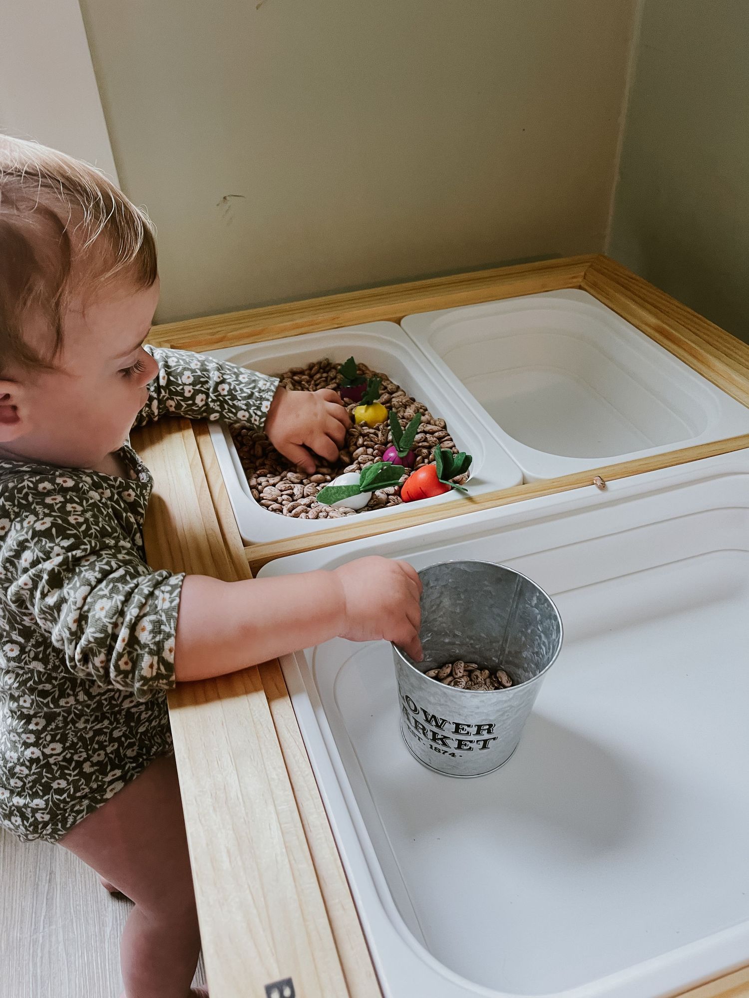 12 month old baby doing a sensory table activity using her Flisat and Bright table  beans, carrots, fruits, and veggies