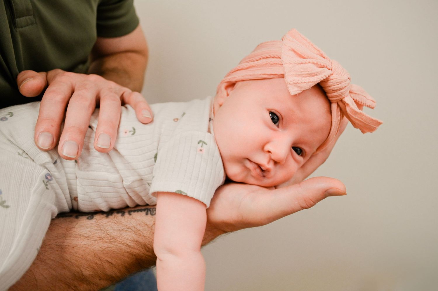 An infant rests peacefully on an adult's supportive hands in a tender moment against a neutral background.