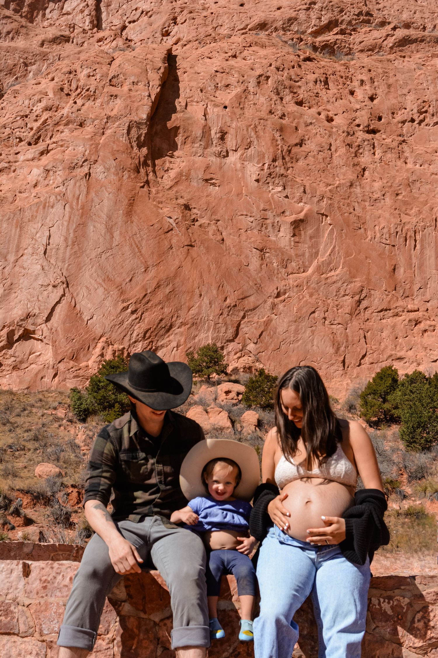 A family sits together on a bench against a red rock canyon wall in the desert.