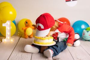 A first birthday celebration setup with Pokemon theme featuring Charmander  colorful balloons on wooden floor while baby puts face in cake