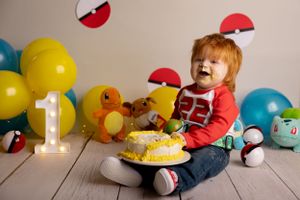 Pokemon themed first birthday party setup with cake, plush toys, balloons and decorations on wooden floor.