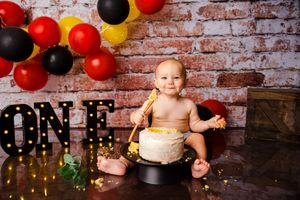 Festive first birthday party setup with red and black balloons against rustic brick wall background.