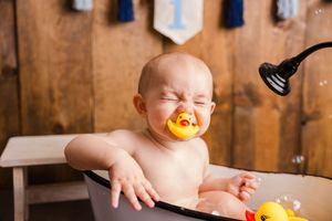 Baby in a bathtub splashes and plays with yellow rubber ducks during bath time.