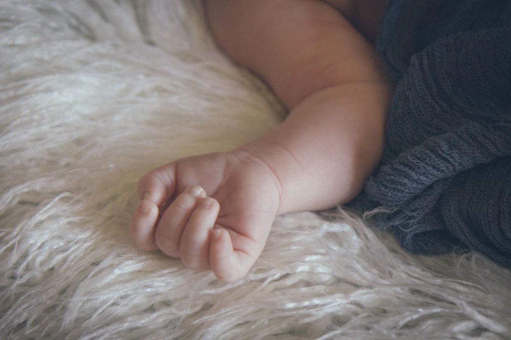 A tiny baby hand rests gently on soft white fur creating a tender and peaceful moment.