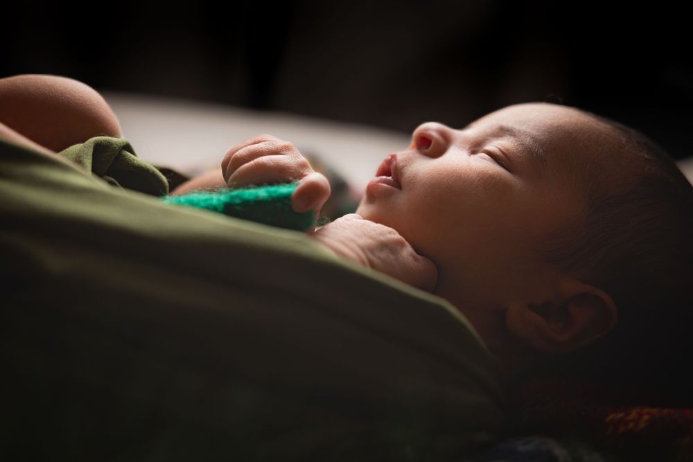 A sleeping baby lies peacefully in soft lighting while holding a small green heart.