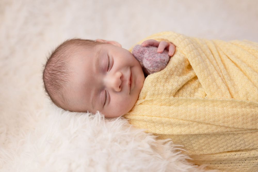 Peaceful newborn baby sleeping swaddled in a soft yellow blanket on a fluffy white fur rug.
