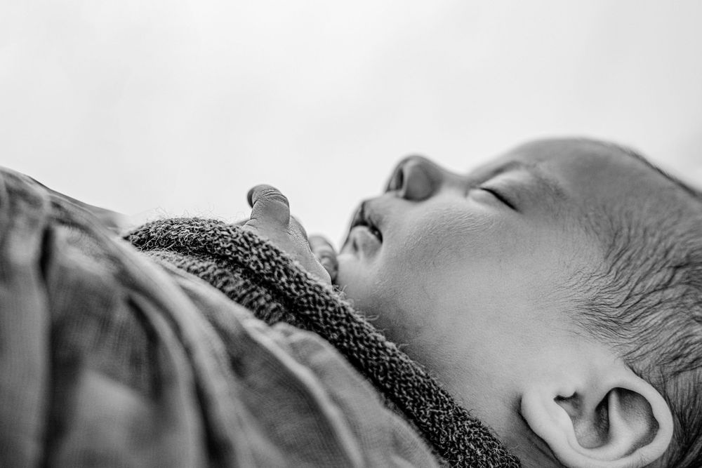 Black and white close-up of a sleeping baby with closed eyes, resting peacefully in soft fabric.