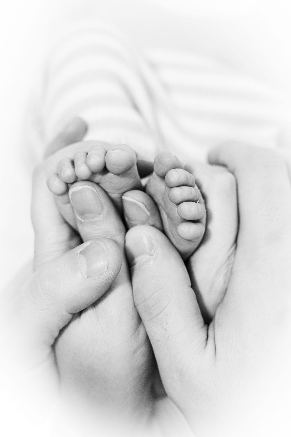 Black and white photo of adult hands gently cradling tiny newborn baby feet, symbolizing love and parenthood.