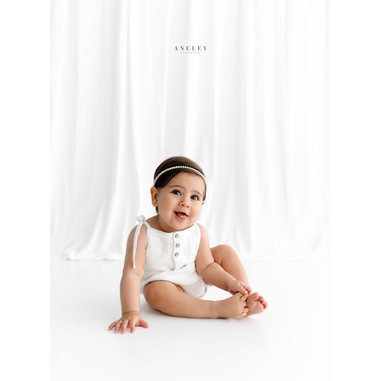 Professional studio portrait of baby in white outfit with pearl headband.