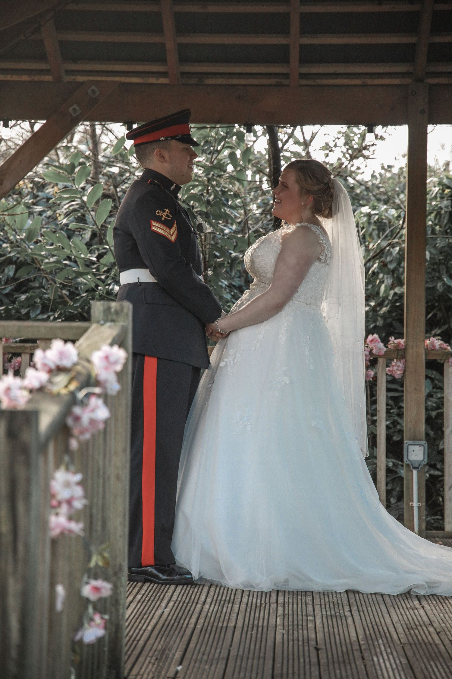 Military wedding ceremony on wooden deck with bride in white gown and groom in formal uniform.