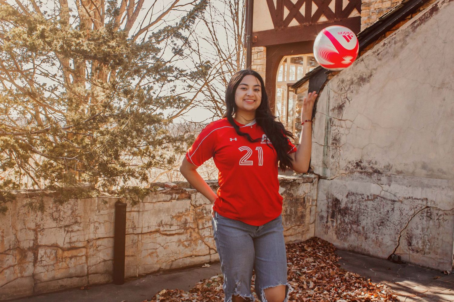 Person wearing red sports jersey number 21 posing against rustic wall in natural lighting.