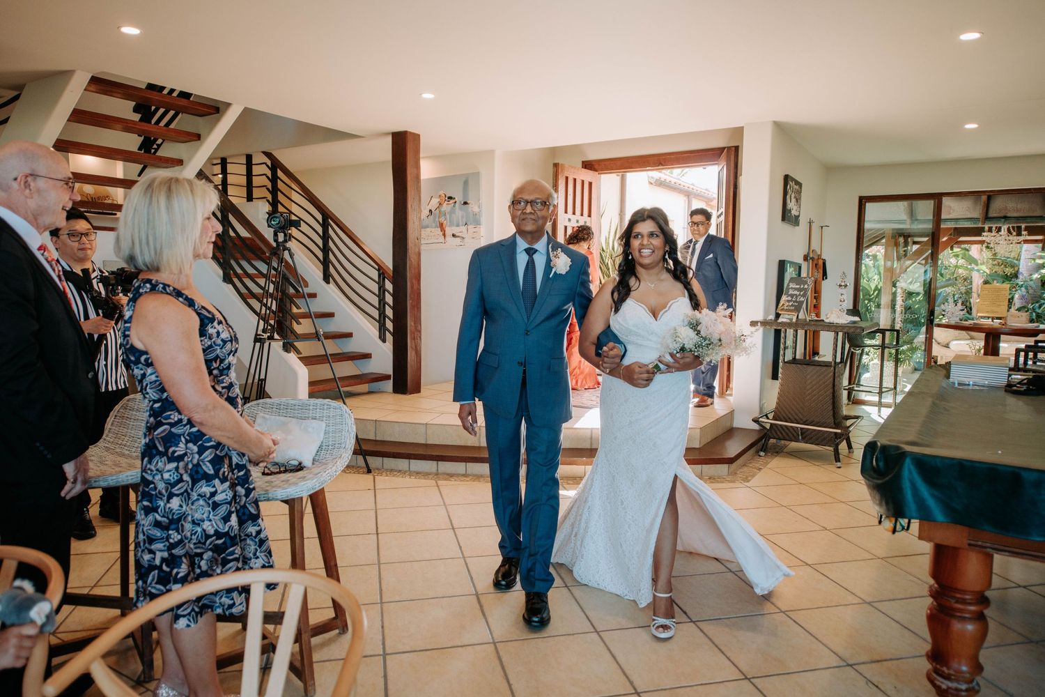 Wedding processional with guests watching in a modern home with staircase.