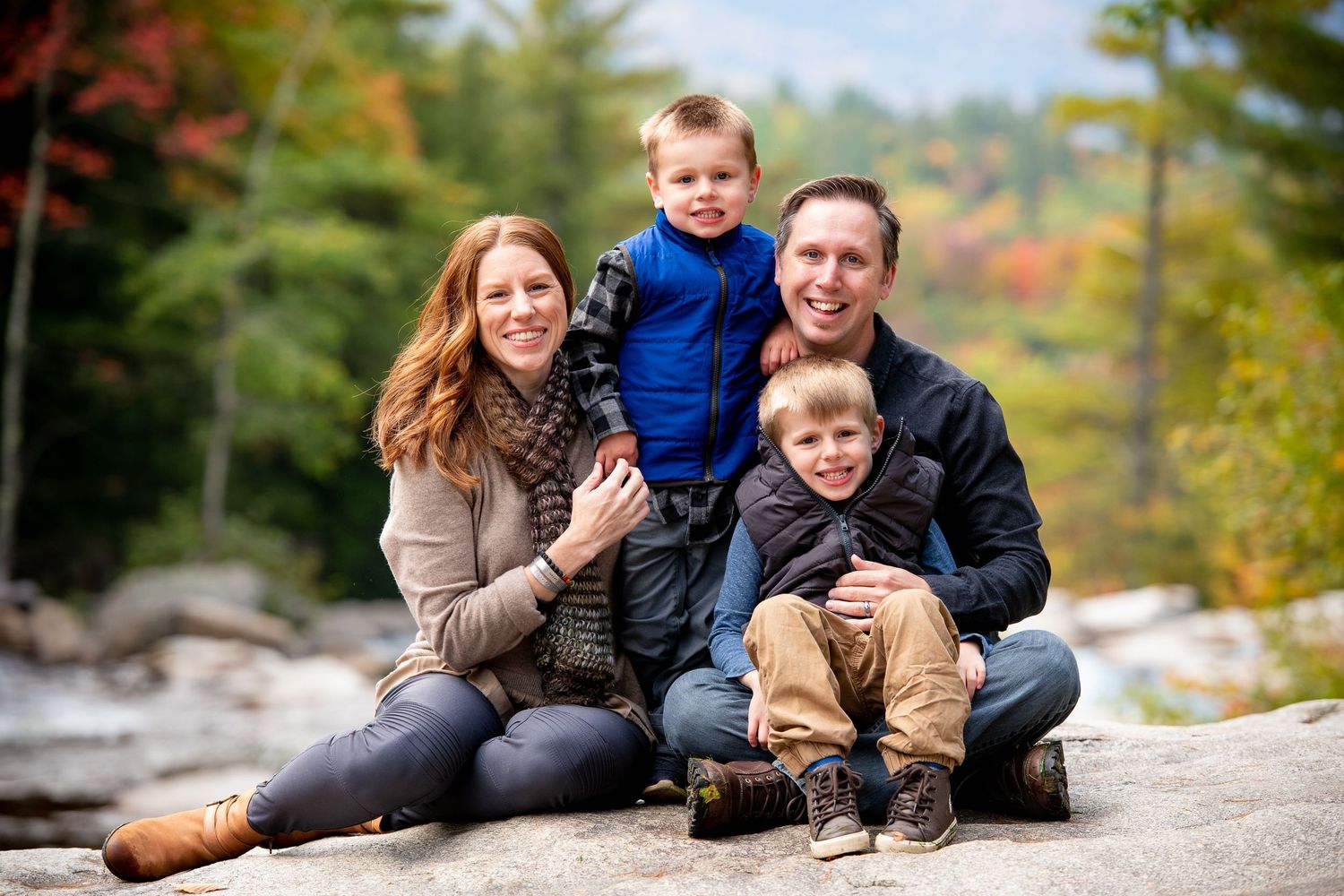 Family poses together on rocky outcrop during autumn foliage session.