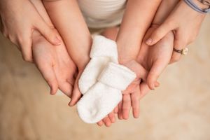 Pair of hands gently holding tiny white baby socks against neutral background.