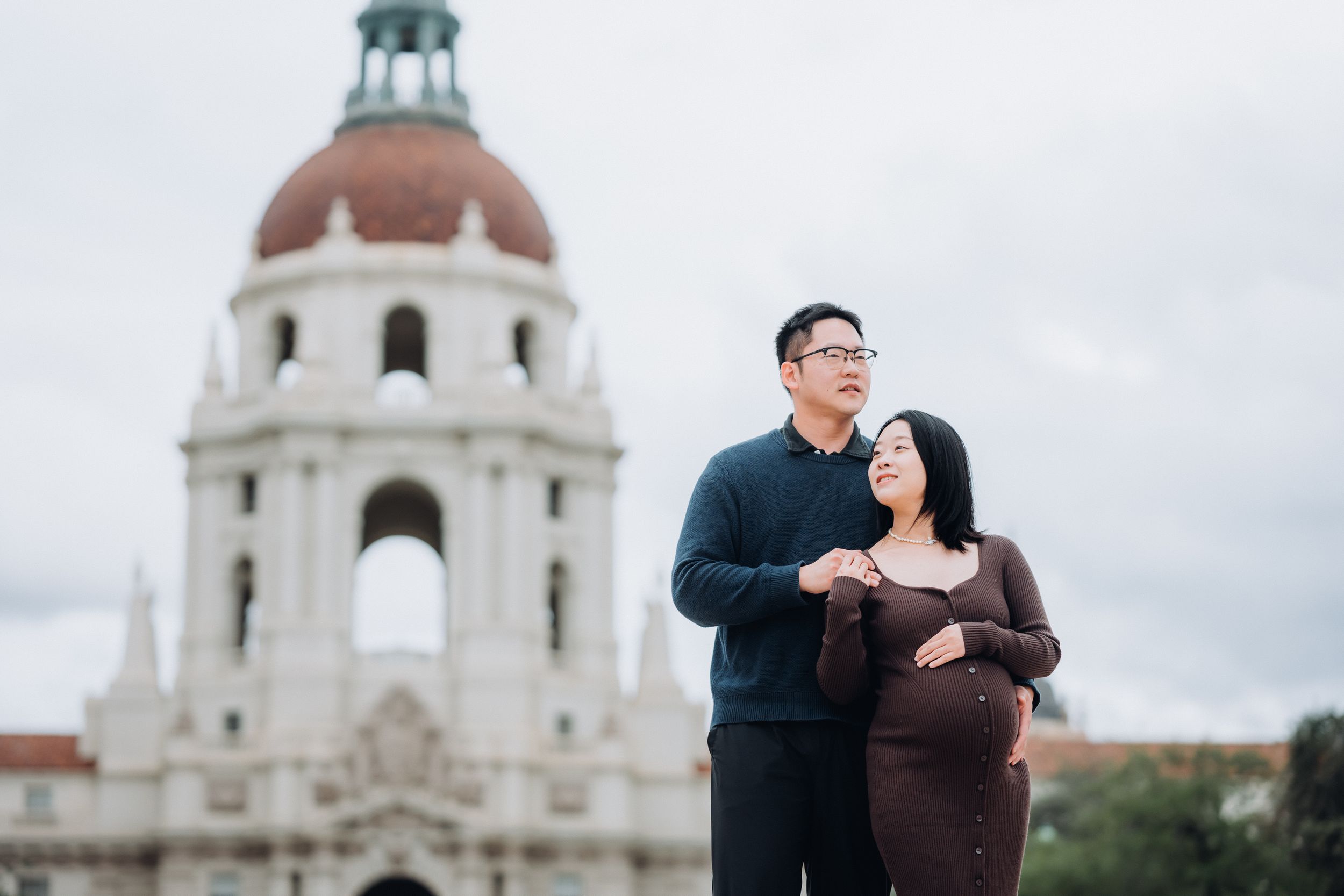 A couple shares a romantic moment in front of a white domed building during an engagement photo session.