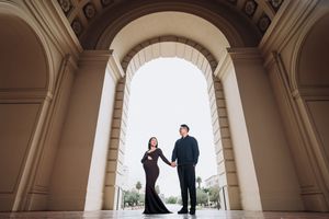 A couple stands in silhouette under a grand arched colonnade with classical architecture details.