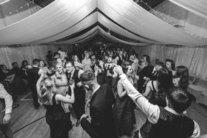 Black and white photo of a large crowd dancing at a wedding reception under a marquee tent.
