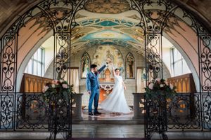 Couple exchanges vows in a beautiful historic chapel with ornate painted walls and wrought iron gates.