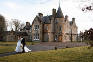 Bride and groom embrace outside a grand Scottish castle wedding venue on a cloudy day.