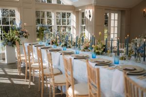 A bright sunlit wedding reception venue with white tablecloths and light blue decor accents throughout the elegant space.