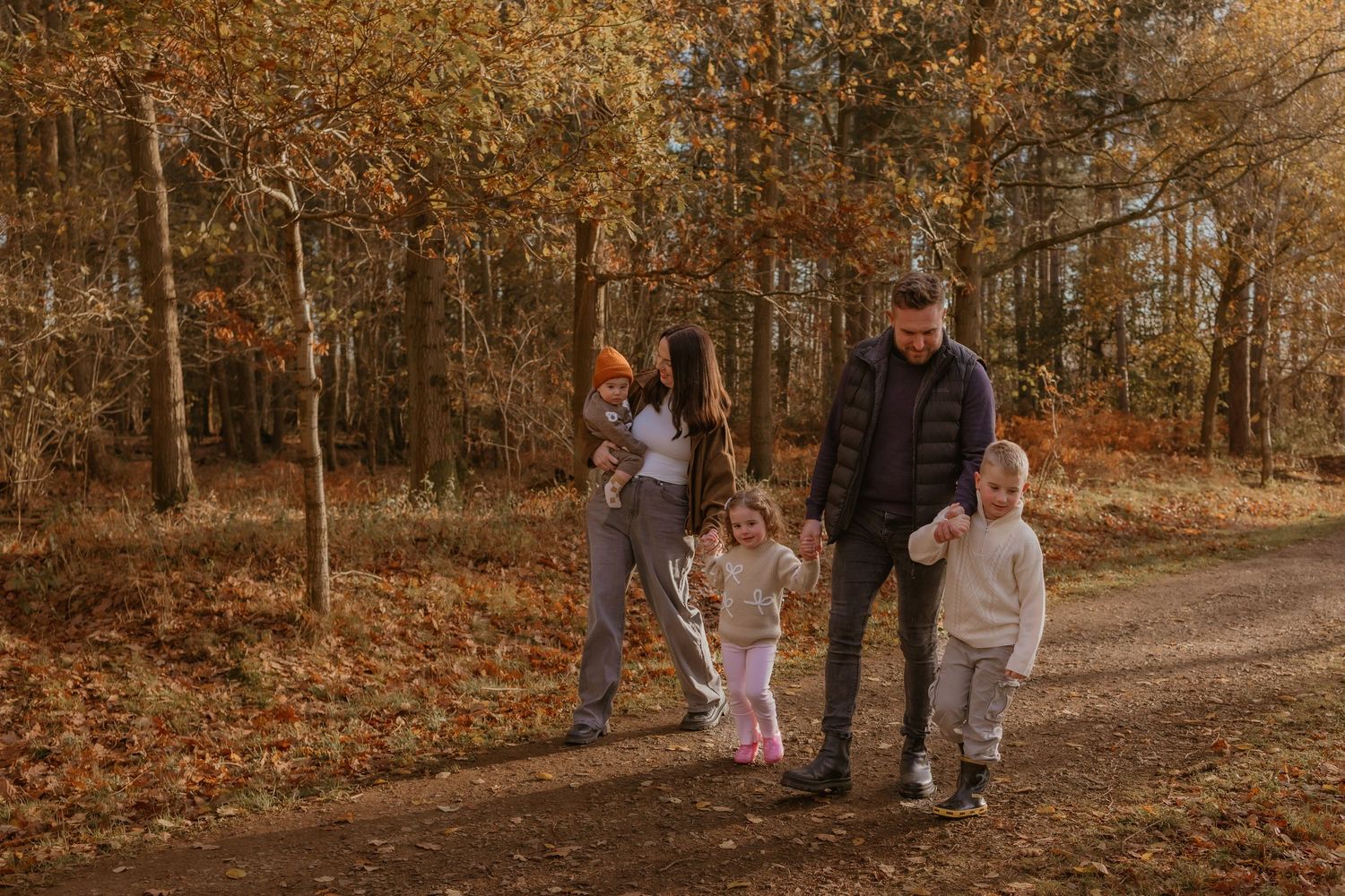 Family walking together through autumn woods with fallen orange leaves.