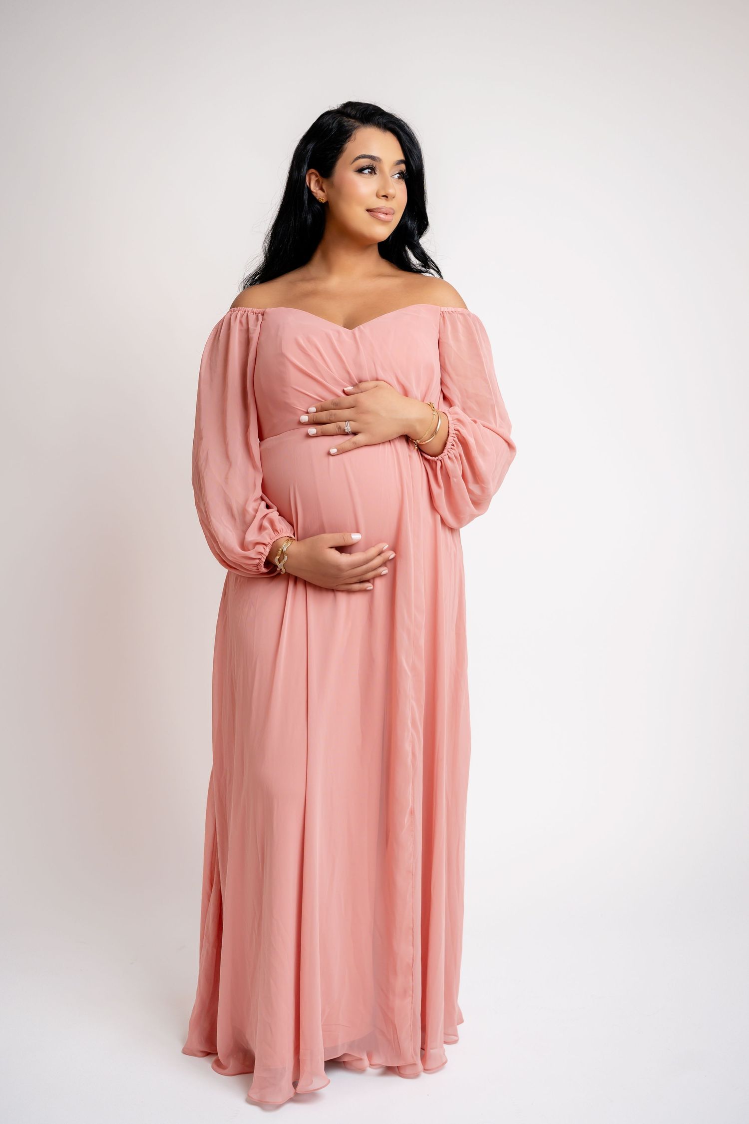 Maternity portraits in flowing pink dress against white backdrop.