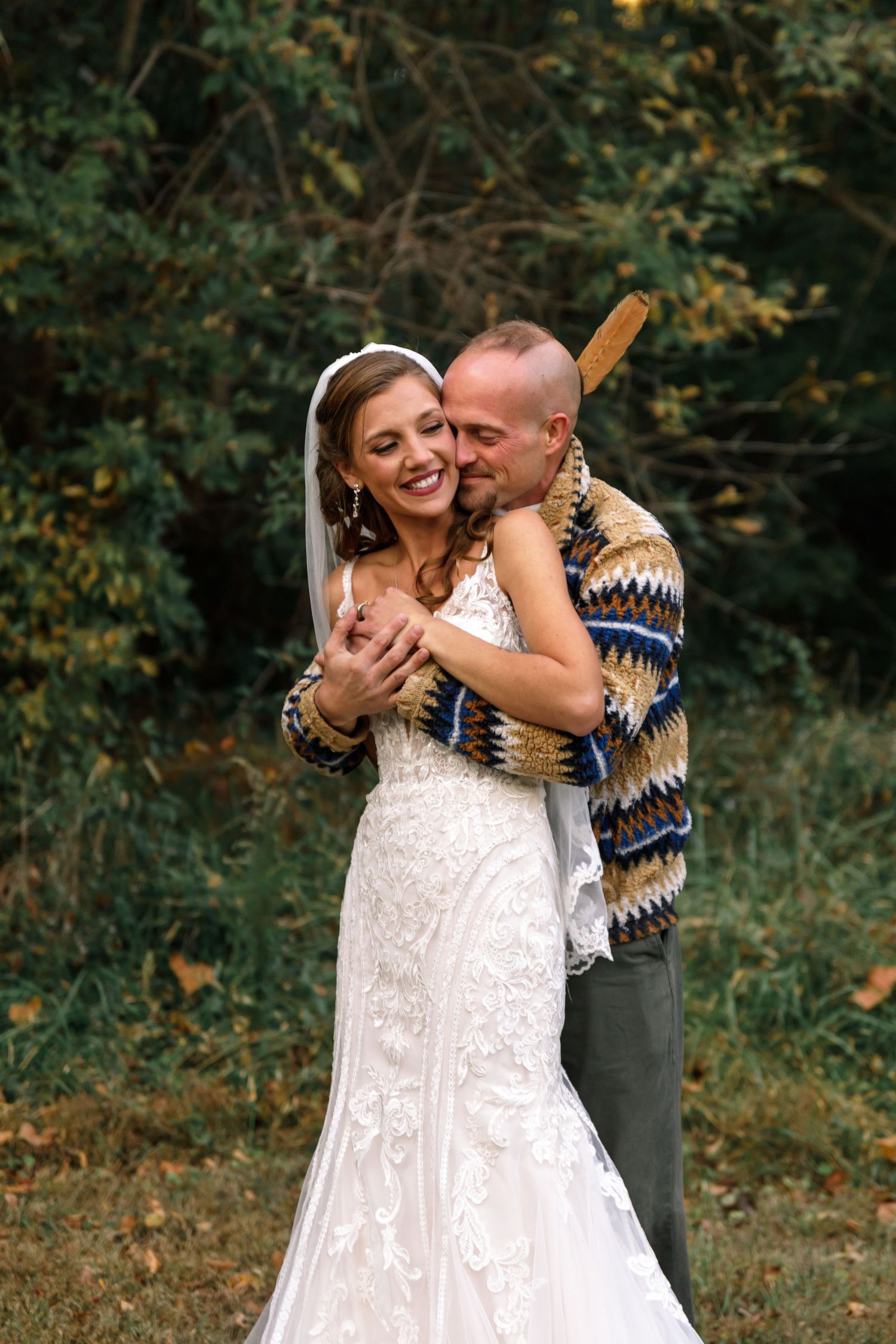 Joyful couple embracing outdoors in wedding attire against autumn foliage.