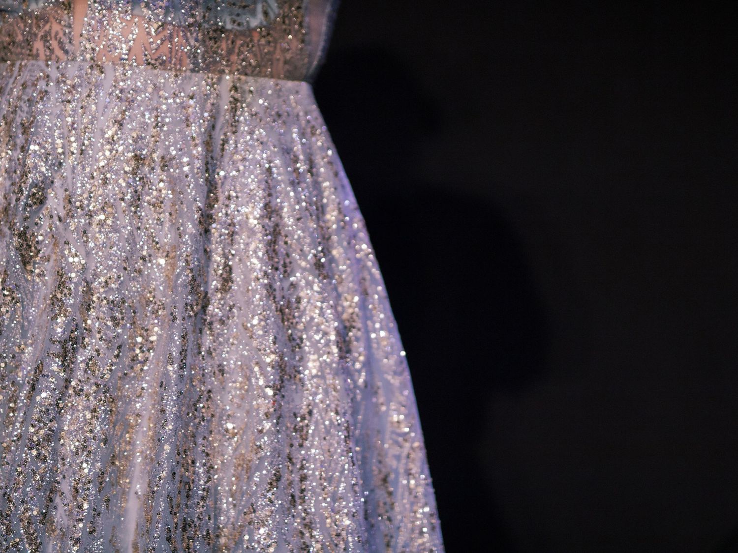 Close-up of sparkly lavender evening gown with sequin details against dark background.