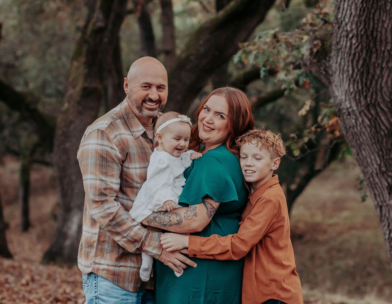 Family portrait in autumn setting with parents and two children among fall trees.