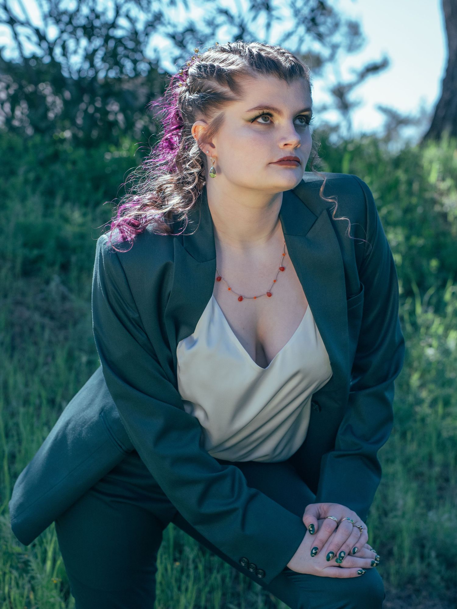 Outdoor portrait in a green field wearing a black blazer and delicate necklace.