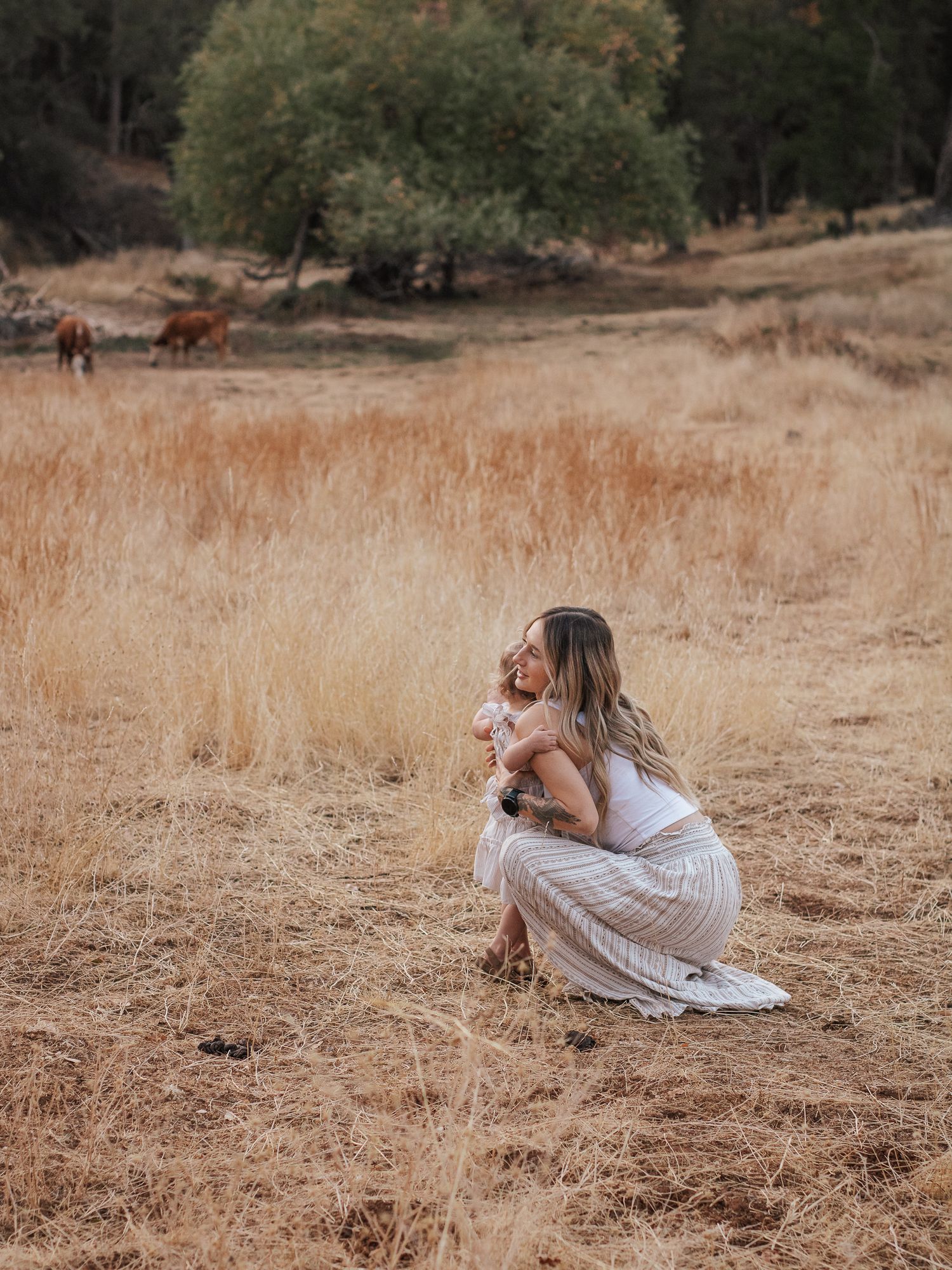 Person in white dress crouches in golden field of dried grass during golden hour.