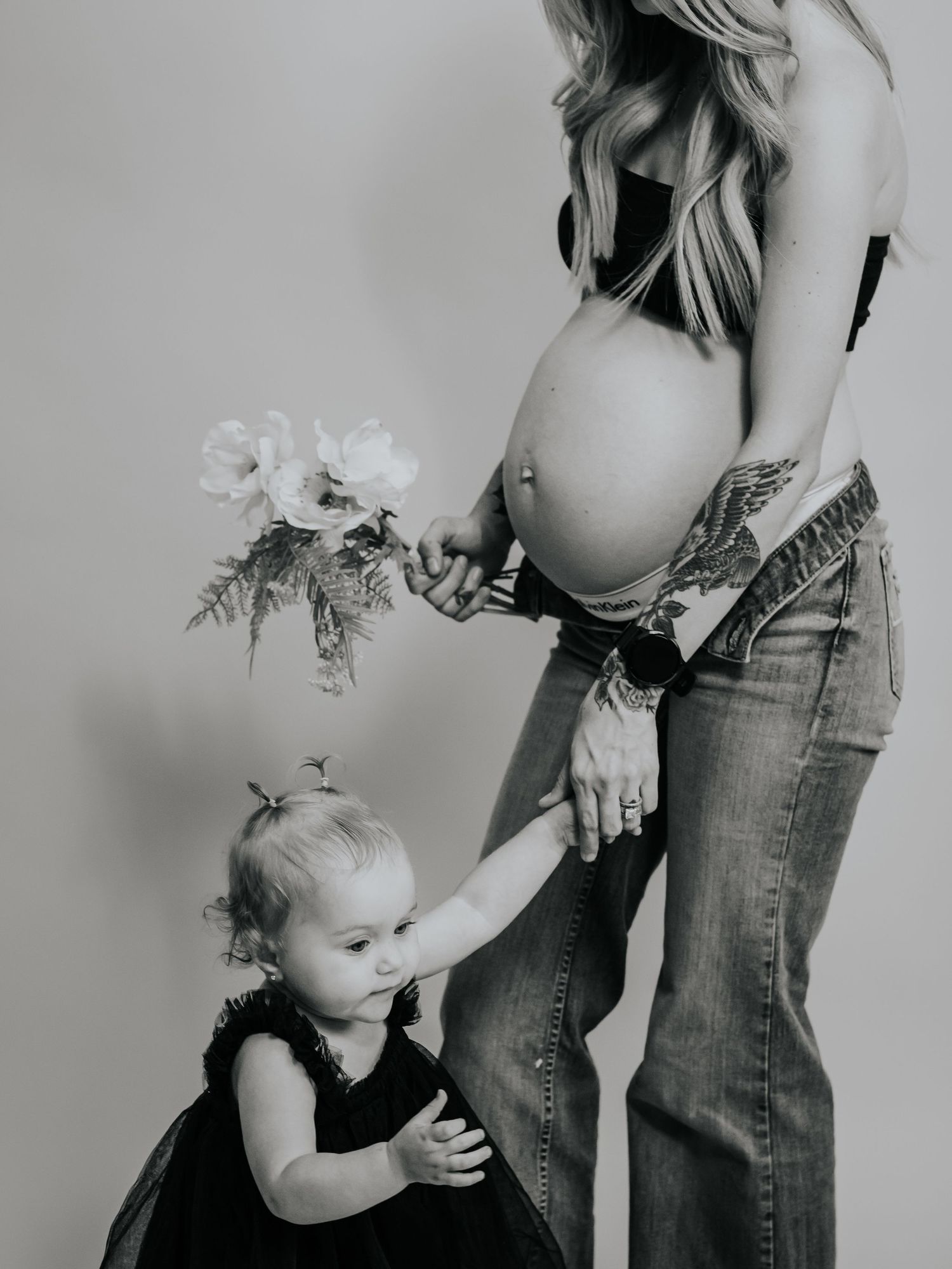 Maternity photo with toddler in black dress reaching for flowers held by mother.