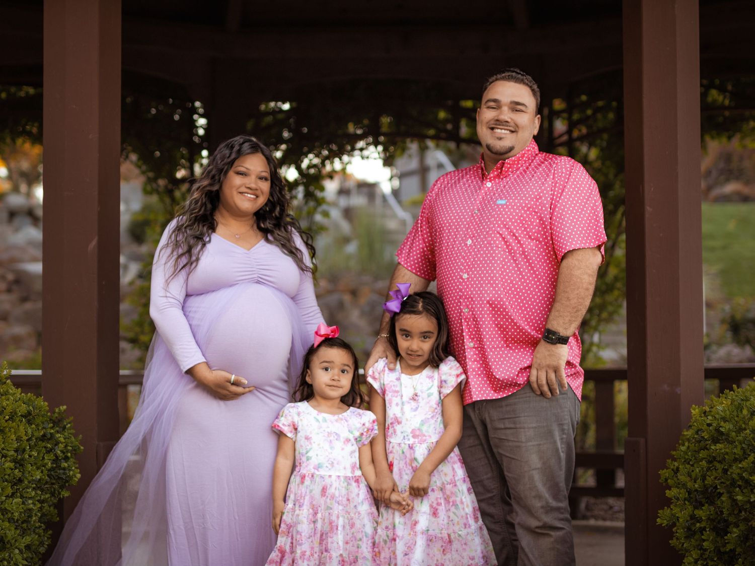 A family portrait under a gazebo featuring parents and two young children in coordinated outfits.