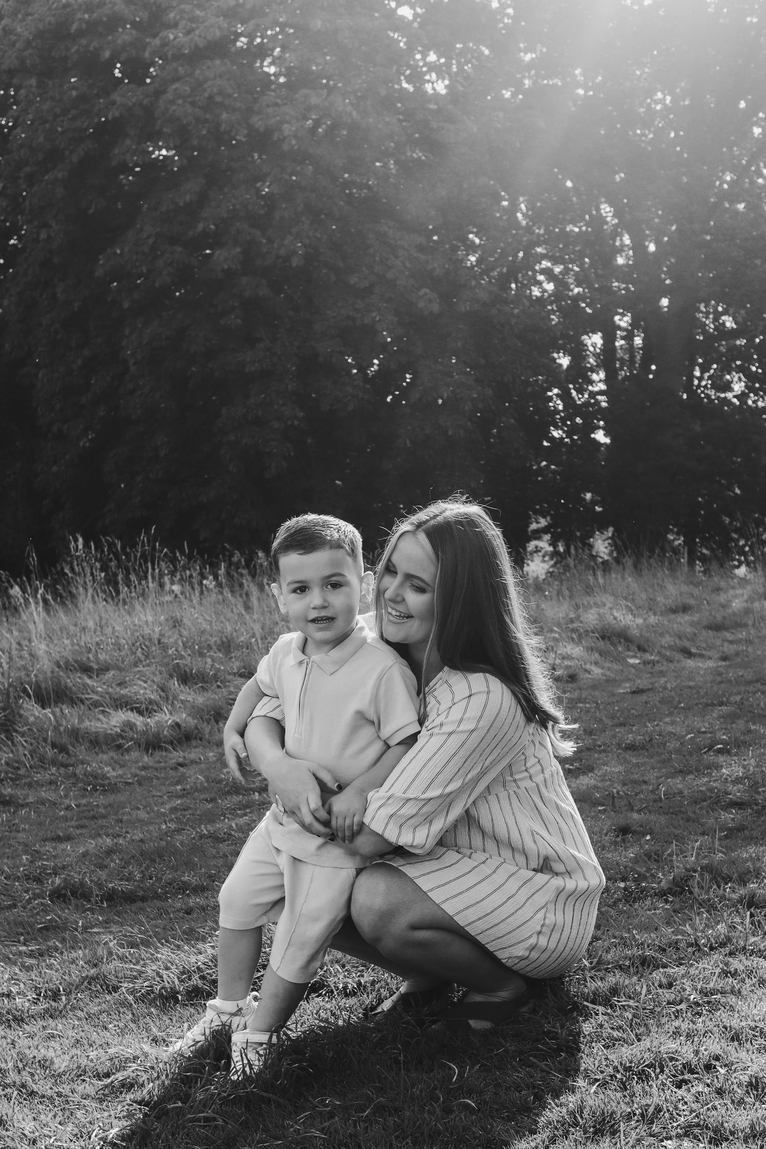 Black and white photo of a tender moment between a mother and child sitting together on grassy hillside.