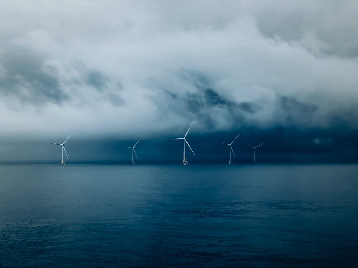 Wind turbines in the ocean under a stormy sky. Photo by Nick Wigmore.