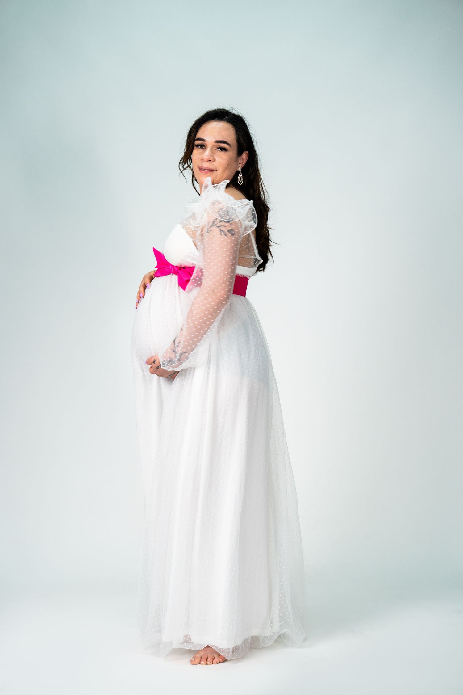 White flowing dress with lace details and pink bow accent photographed against light background.