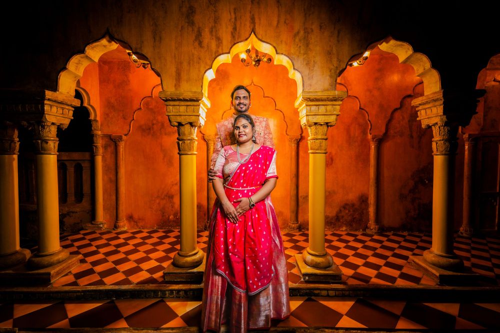 A couple poses in formal attire under ornate golden arches with dramatic lighting.